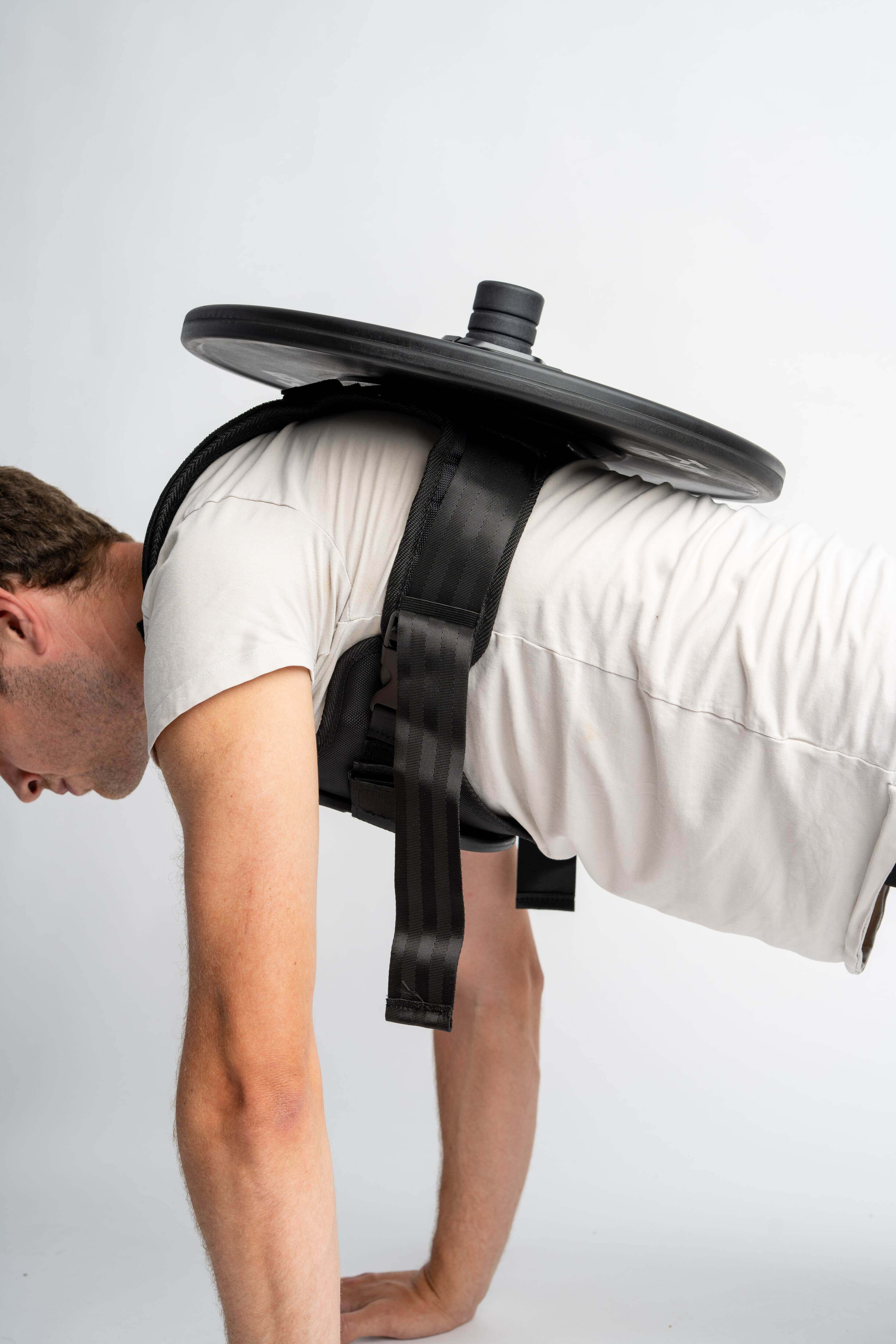 Man in push-up position wearing an adjustable weight vest with a weight plate for strength training.